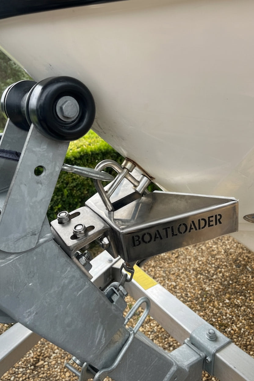 Close-up of a boat trailer hitch assembly with a metal receiver and a black wheel, branded BOATLOADER Launch and Retrieve system, set against a white boat hull and outdoor ground background.