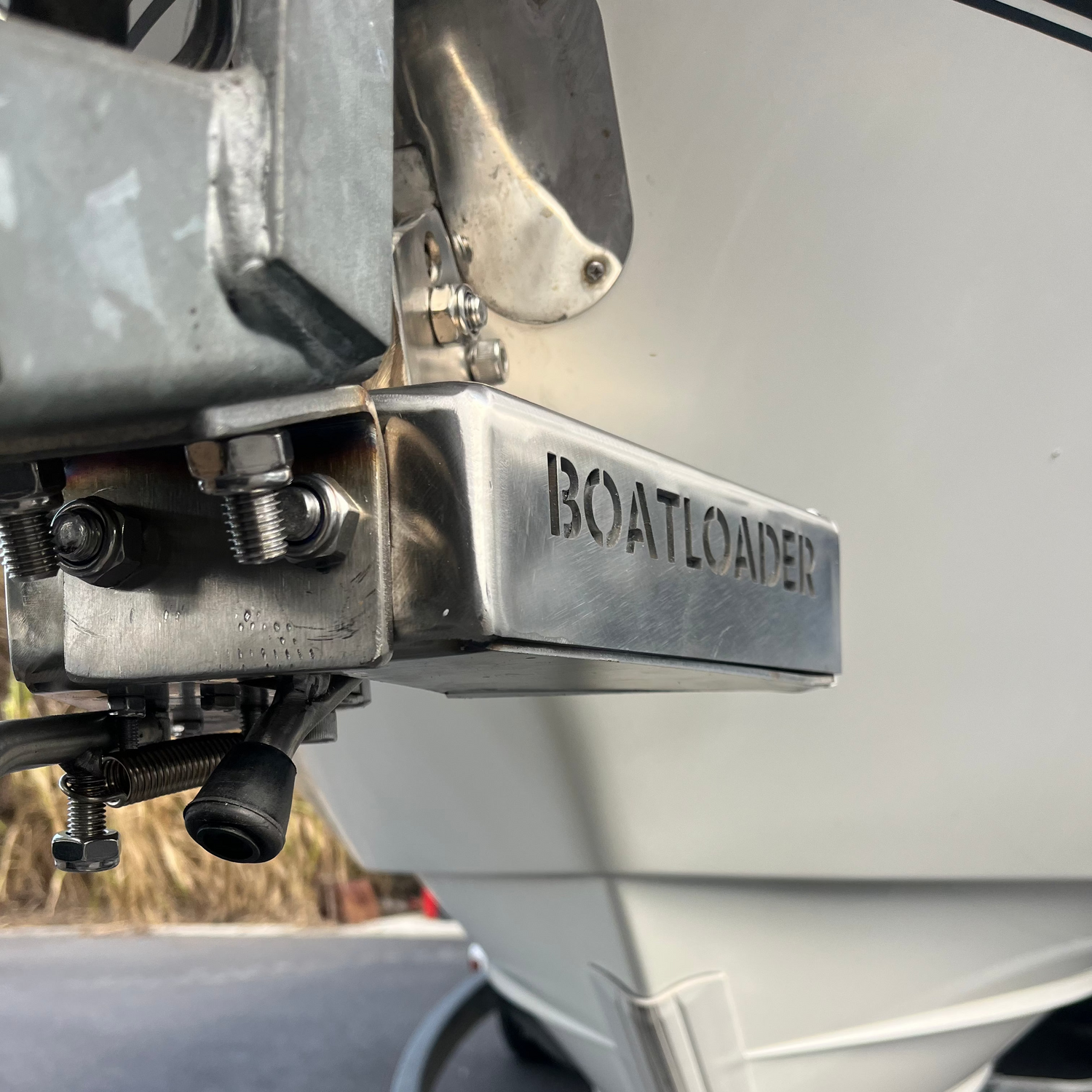 Close-up of a Boatloader metal trailer hitch receiver mounted on a white boat trailer, with part of the boat hull, trailer frame, and tire visible outdoors.