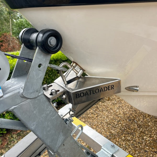 Close-up of a boat trailer hitch assembly with a silver metal receiver and a black roller, branded BOATLOADER, attached to a white boat hull outdoors.